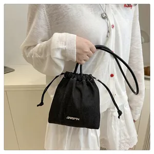Détail du sac seau en denim noir avec fermeture à cordon et logo en métal
