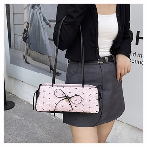 Sac baguette plissé rose avec nœuds noirs et breloque cœur porté par un mannequin en ville