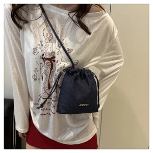 Détail du sac seau en jean bleu avec cordon, montrant la texture et le logo en métal