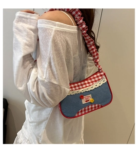 Detail of red plaid shoulder bag with white lace trim and cherry embroidery accents