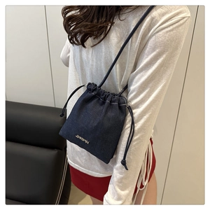 Dettaglio della borsa a secchiello in denim blu scuro con logo in metallo e trama su modella