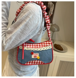 Detalle del bolso de hombro denim azul con ribete de cuadros rojos y bordado floral