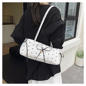 Détail du sac baguette plissé blanc avec motifs de nœuds noirs et pendentif en forme de cœur