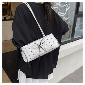 Détail d'un sac à bandoulière plissé blanc avec des nœuds noirs et un pendentif en cœur