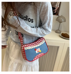 Detail of blue denim and red plaid crossbody bag with lace edges and cherry embroidery