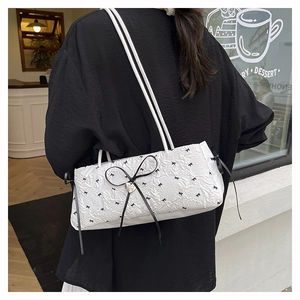 Détail du sac à épaule texturé blanc avec imprimé nœud noir et pendentif cœur