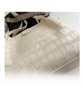Close-up of white crocodile pattern faux leather with gold rivets and woven shoulder strap