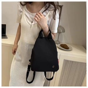 Mini black nylon backpack showing a side view with a red label in a home setting