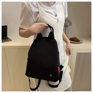 Close-up of black nylon mini backpack featuring red fashion tag and metallic logo
