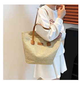Detail of hand-woven straw tote bag with brown leather handles and logo patch