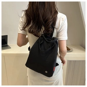 Detailed view of casual black canvas backpack with metal M logo and woven red label