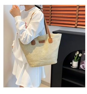 Detailed view of a large straw tote bag with brown leather handles worn by a model