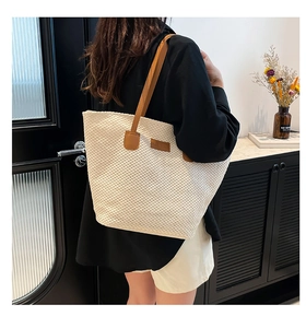 Detail of a beige woven tote bag with brown leather straps and a minimalist logo patch