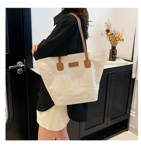 Detail of a large cream woven tote bag with brown leather straps worn on the shoulder