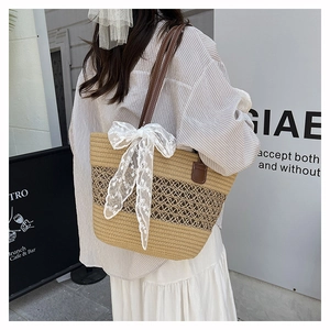 Detail of straw tote bag featuring white lace bow and brown leather shoulder straps