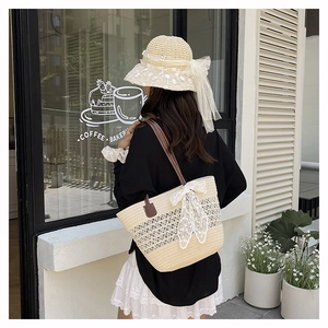 Straw tote bag with lace bow and sun hat shown on a model in a cozy outdoor cafe setting