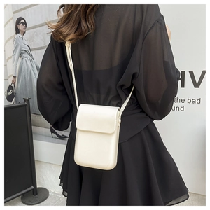 Vertical off-white crossbody phone bag with flap closure on a model wearing black