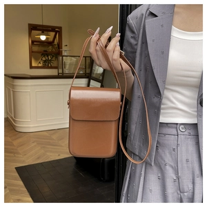 Bolso bandolera vertical marrón de piel sintética en un entorno de café cálido