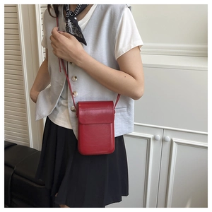 Vertical red glossy leather crossbody phone bag shown on model in a minimalist setting