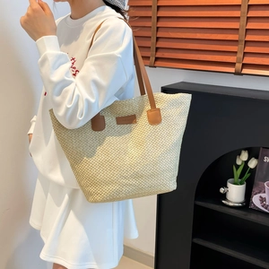 Large straw tote bag with brown leather straps and fashion label for summer beach use