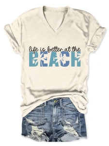 Flat lay of cream V-neck beach t-shirt paired with distressed denim shorts and palm tree print