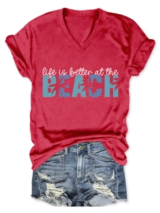 Detail of red V-neck T-shirt with beach text print paired with distressed denim shorts