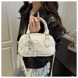 White vintage boston bag with pearl bow charm held by model in a minimalist setting