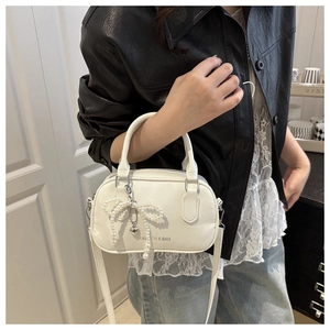 Close-up of white leather pillow bag with pearl bow, heart pendant and printed text detail
