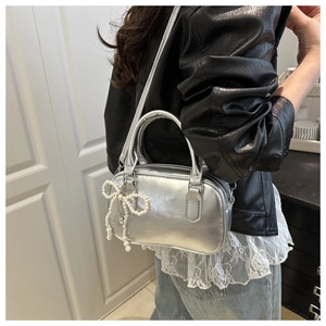 Detail view of silver pillow bag featuring pearl bow charm and sleek fashion logo