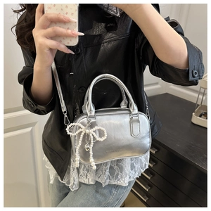 Detail of silver metallic square bag with pearl bow charm and crossbody strap
