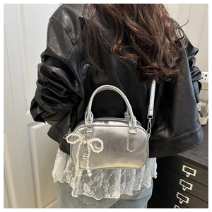Detail of silver metallic handbag with pearl bow charm worn over a black leather jacket