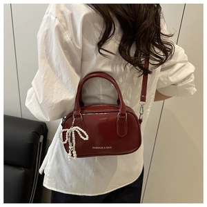Close-up of burgundy oil wax leather bag with pearl bow charm and shoulder strap