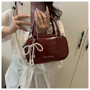 Detail of burgundy glossy leather handbag featuring pearl bow charm and logo printing