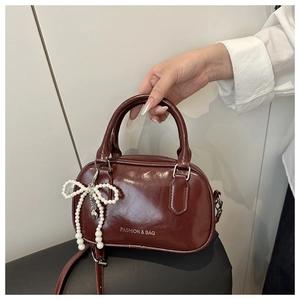 Detail of burgundy glossy leather handbag featuring pearl bow charm and fashion lettering