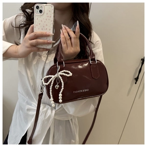 Close-up of wine red patent leather handbag with pearl bow charm and shoulder strap