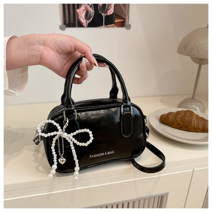 Detail of black glossy bowling bag featuring a pearl bow charm and heart pendant