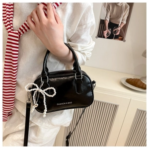 Detail of black glossy handbag featuring fashion text and pearl bow charm accessory