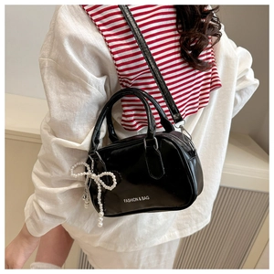 Close-up of black glossy leather bowling bag with pearl bow and fashion branding