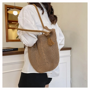 Side view of a brown woven tote bag with crochet details and a fringe tassel on model