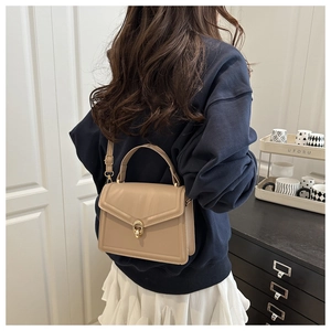 Détail latéral du sac bandoulière en cuir beige avec poignée et fermoir rotatif doré