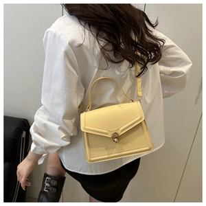 Détail d'un sac à main en cuir PU jaune clair avec boucle dorée porté par un modèle