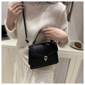 Détail d'un sac à main trapèze noir avec boucle dorée et bandoulière sur un mannequin