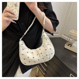 Détail du sac croissant plissé blanc avec broderie de nœuds noirs et bandoulière perle