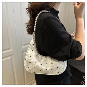 Vue détaillée d'un sac à épaule matelassé blanc avec nœuds noirs et sangle en perles