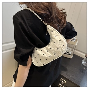 Détail du sac croissant blanc avec motifs de nœuds noirs et bandoulière en perles