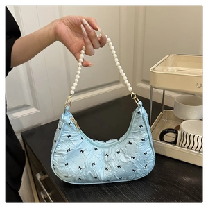 Détail du sac croissant bleu clair avec nœuds noirs et bandoulière en perles blanches
