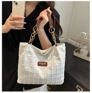 Detail van witte tweed shopper met bruine lederen handvatten en een gouden kettingaccent