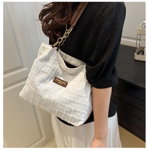 Detail of white tweed tote bag featuring textured fabric and gold metal chain strap