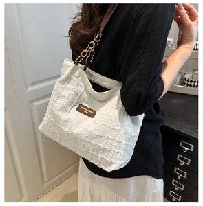 Detail of white textured tote bag with gold chain strap and leather logo tag