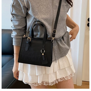 Detail of black crocodile embossed leather tote bag with gold hardware and shoulder strap